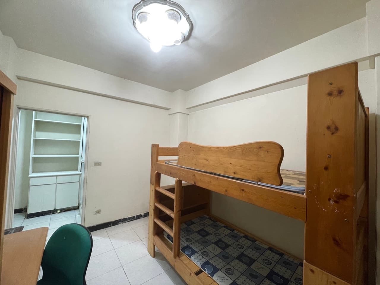 Room with a wooden bunk bed, desk and the door to the private bathroom