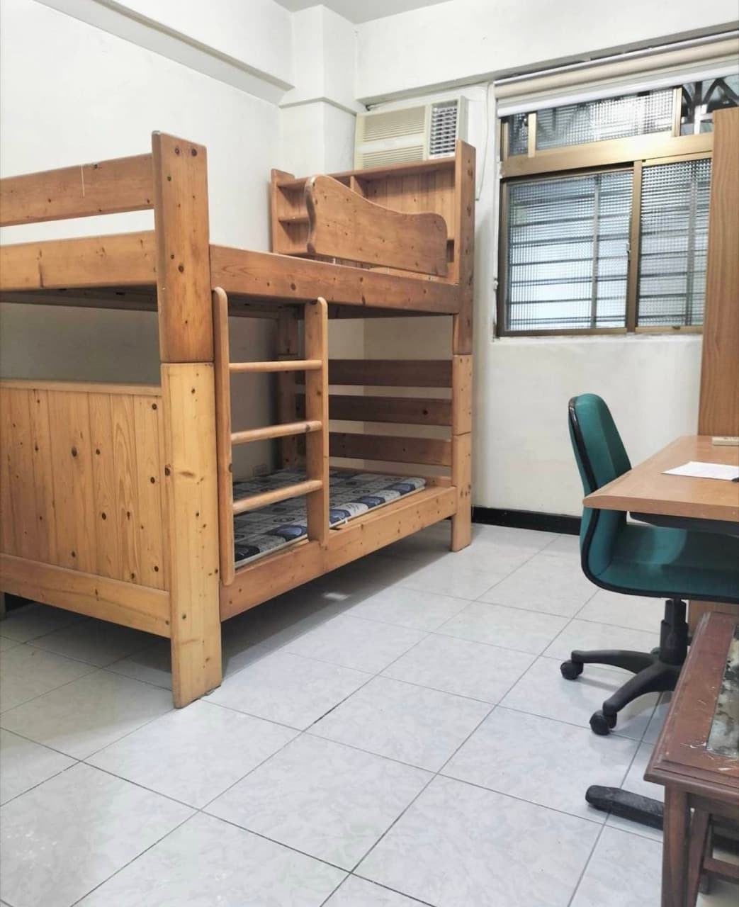 Room seen from the bed side, with window, air conditioner, desk and chair