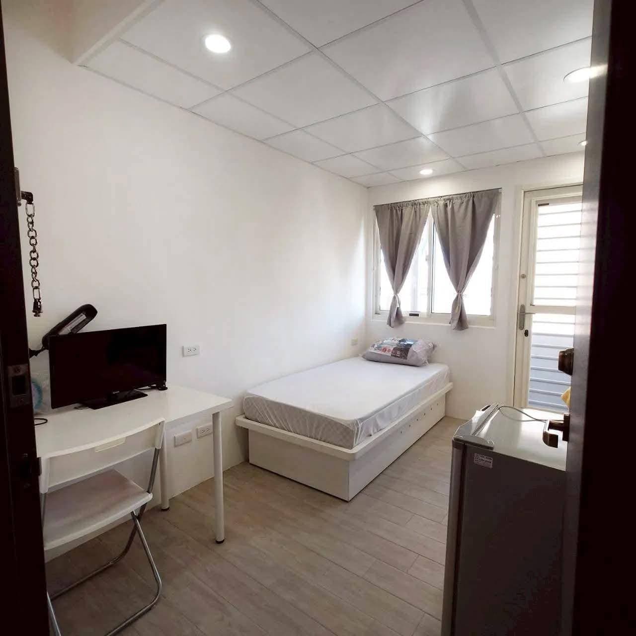 Room seen from the doorway, with desk, TV and mini fridge